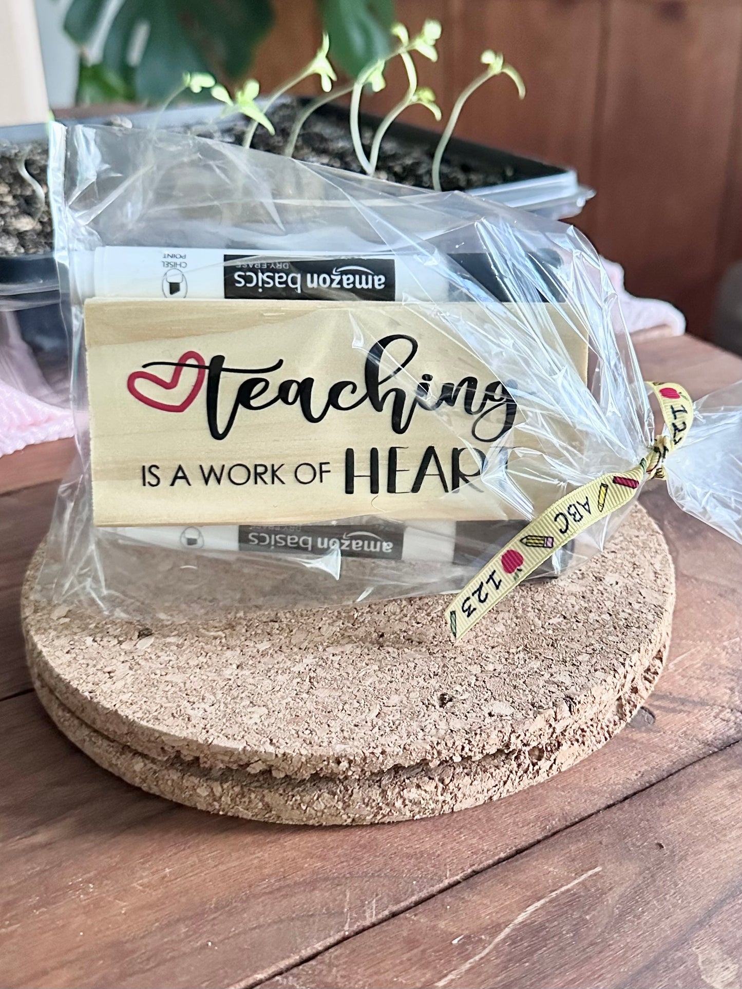 Packaged 'Teaching is a Work of Heart' style teacher eraser kit placed on a cork trivet on a wooden surface
