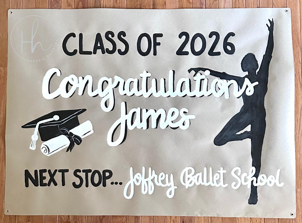 A personalized graduation banner displayed flat on a wooden floor. The banner is beige with black and white printed text and graphics, including 'Congratulations James', 'Class of 2026', 'Next Stop.