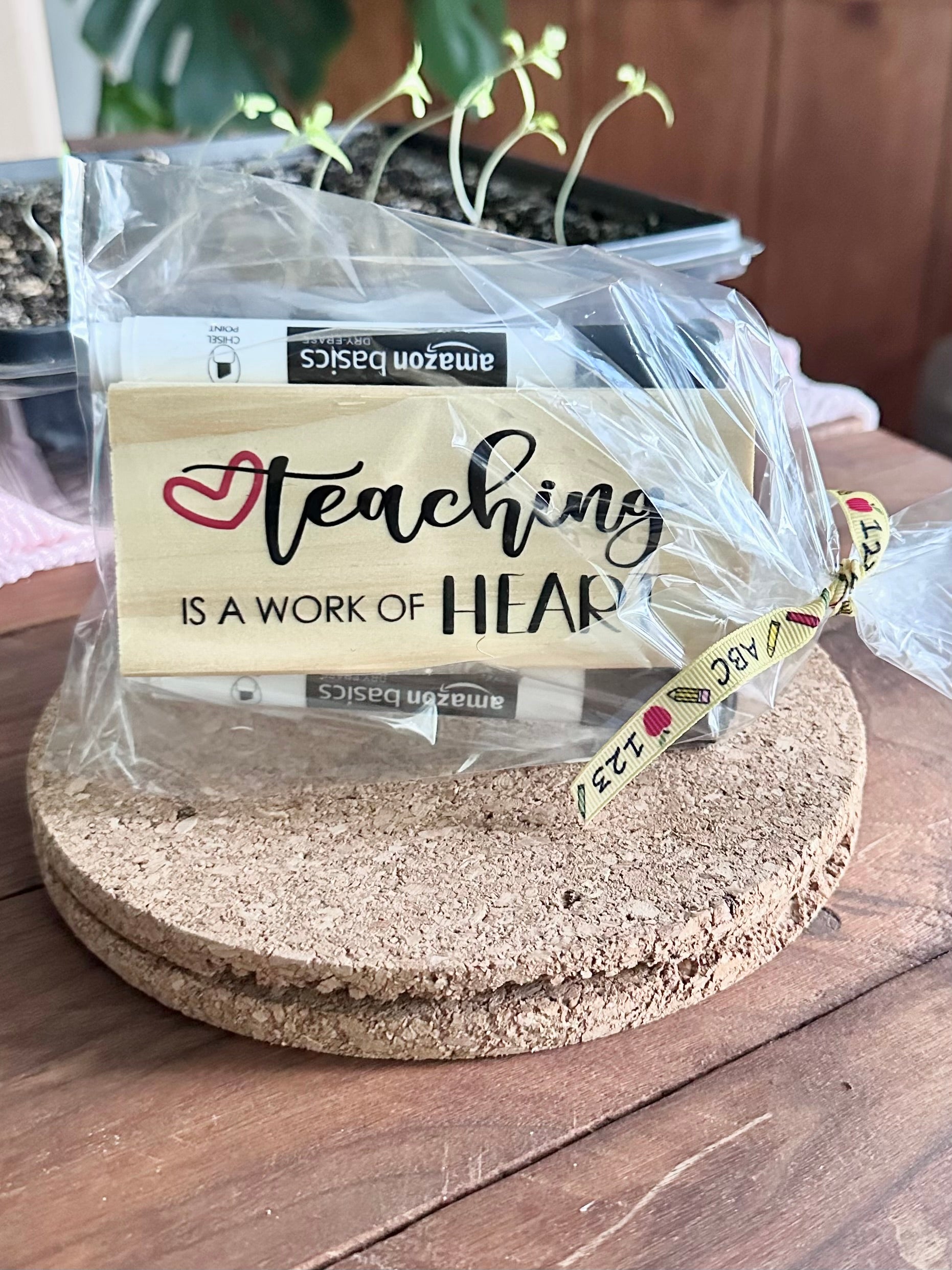 Packaged 'Teaching is a Work of Heart' style teacher eraser kit placed on a cork trivet on a wooden surface