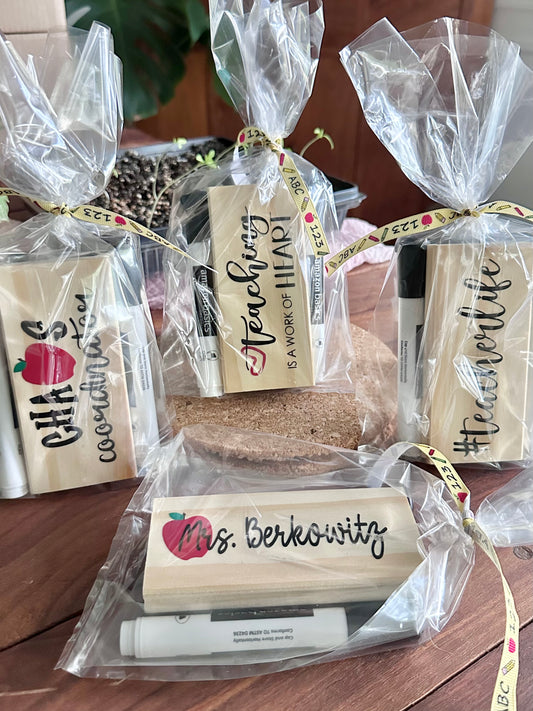 Packaged 'Chaos Coordinator,' 'Teaching is a Work of Heart,' '#teacherlife,' and teacher name style teacher eraser kits placed on a cork trivet on a wooden surface